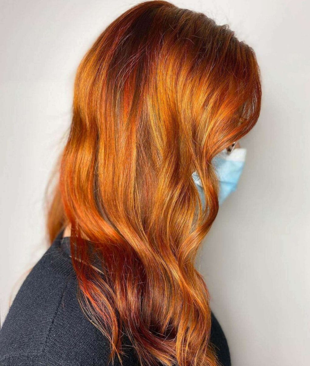 Warm red balayage on layered waves, showcasing rich tones.