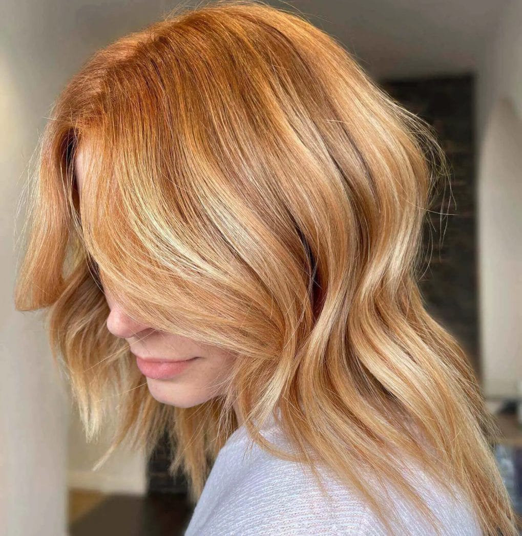 Subtle red balayage highlights on warm blonde hair with soft curves.