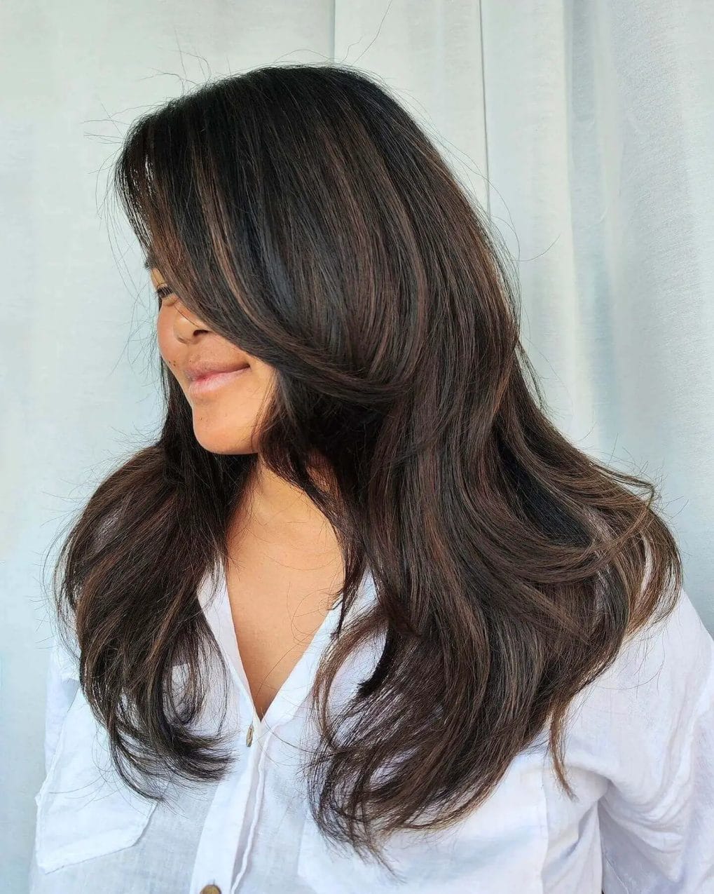 Sun-kissed brunette with dimensional layers, airy blowout style.