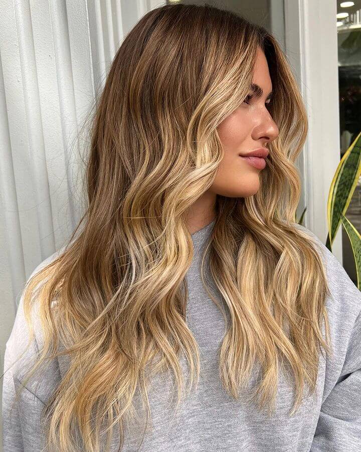Sun-kissed balayage with honey and caramel tones blending into blonde ends, styled in tousled waves