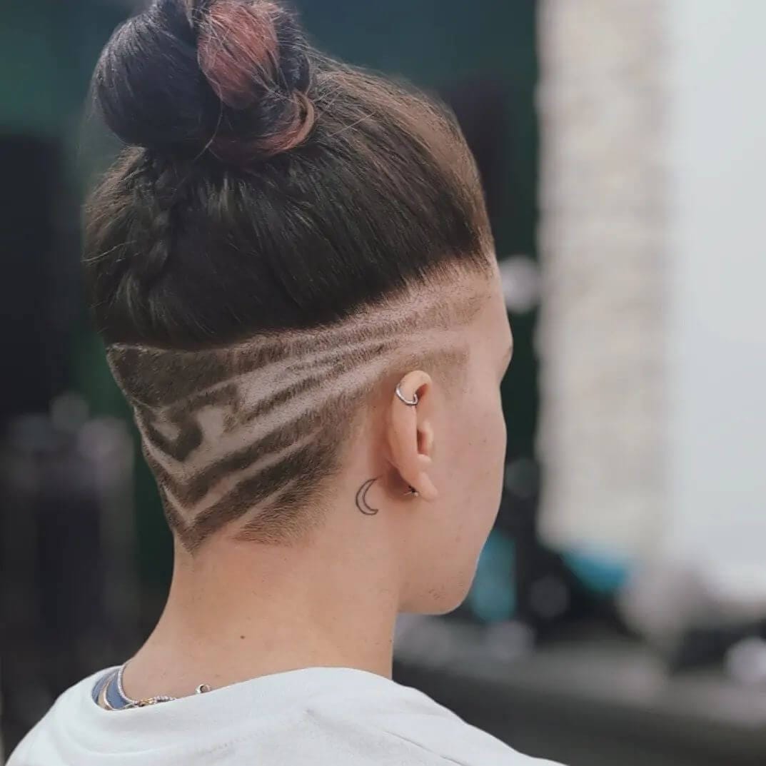 A topknot sitting over an undercut with waved and straight line designs.