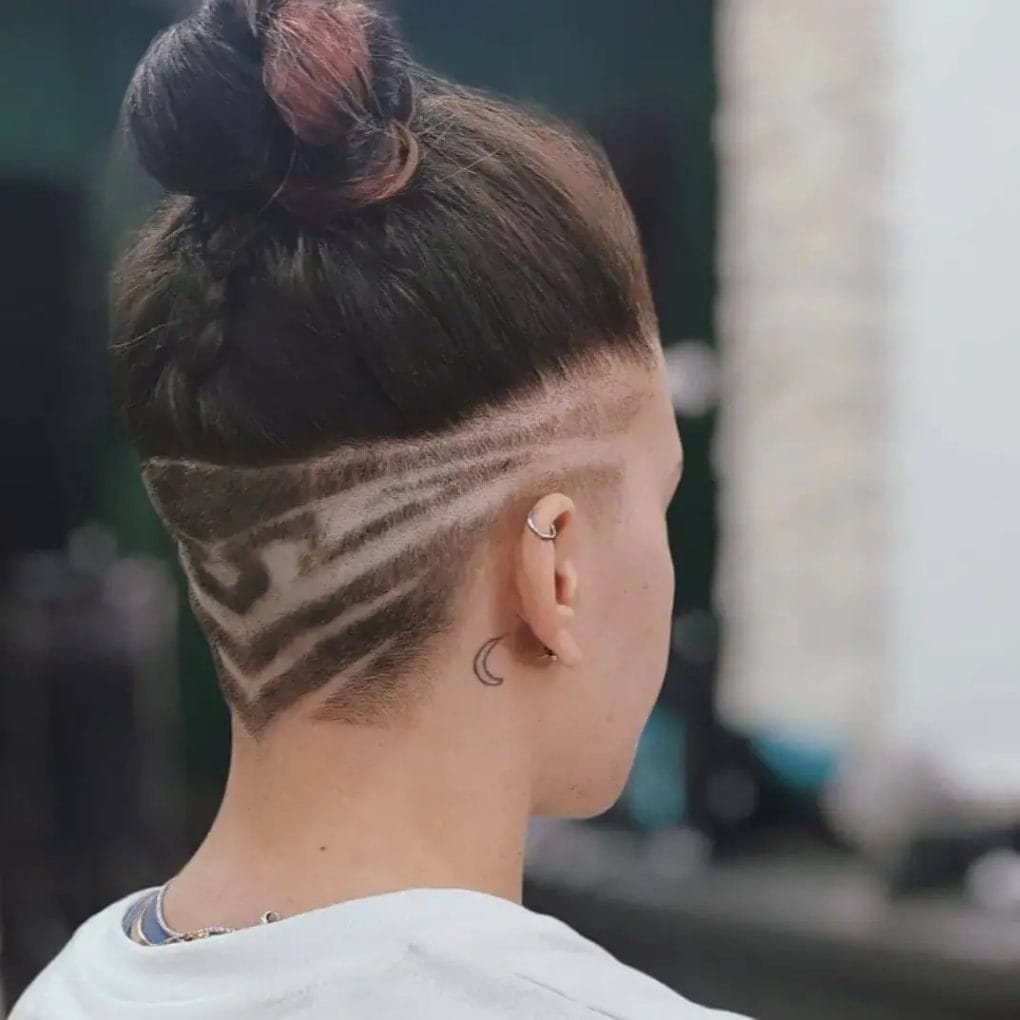 A topknot sitting over an undercut with waved and straight line designs.