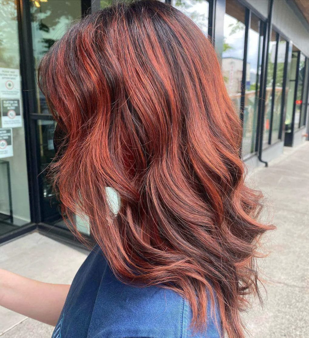 Brunette to vibrant copper balayage, mid-length wavy layers.