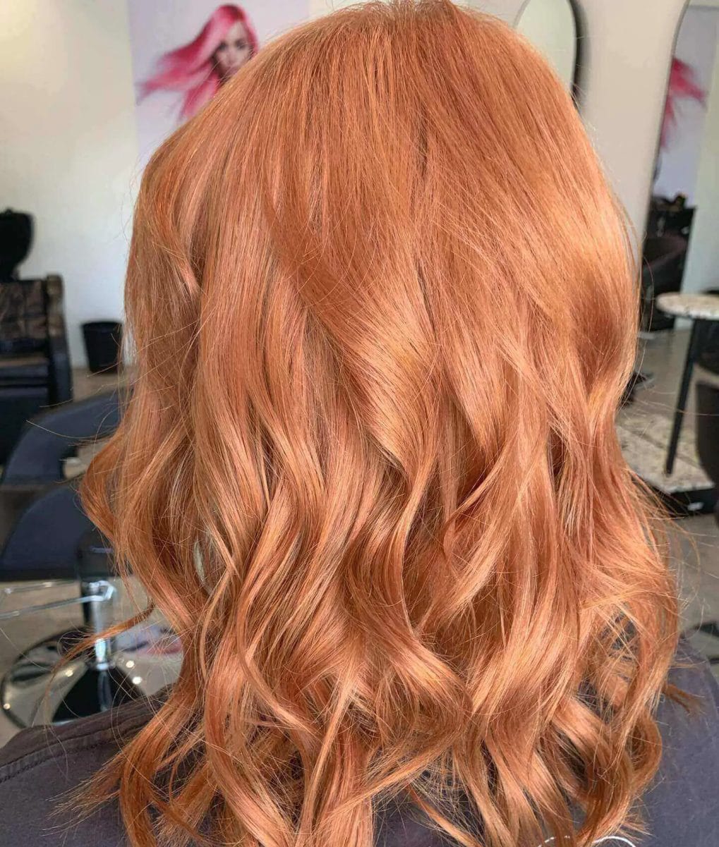 Warm red balayage on a blonde base with vibrant wavy layers.
