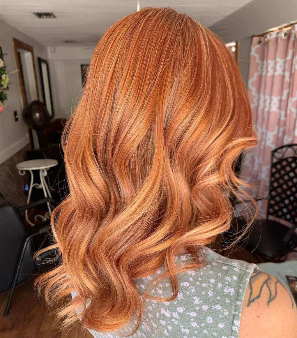 Warm blonde to vibrant red balayage on long, wavy layers.