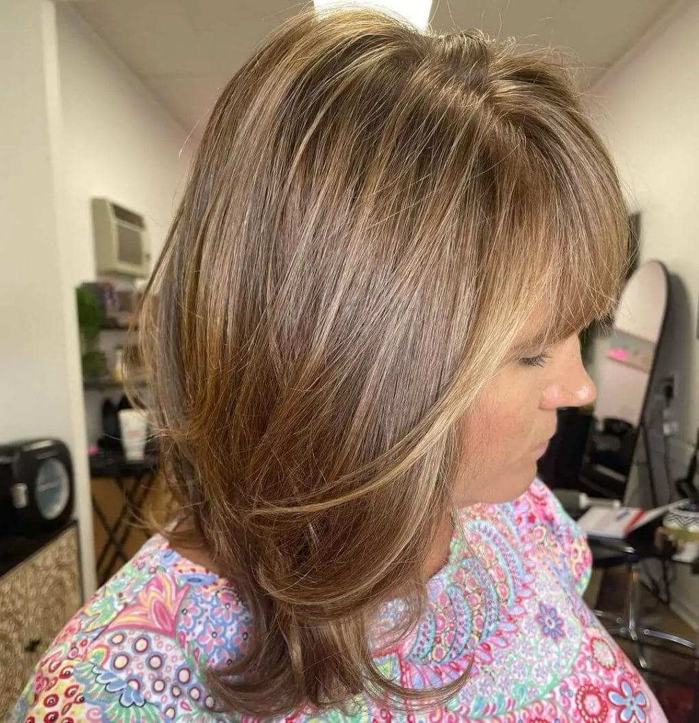 Warm brown layered haircut with subtle highlights and side-swept bangs.
