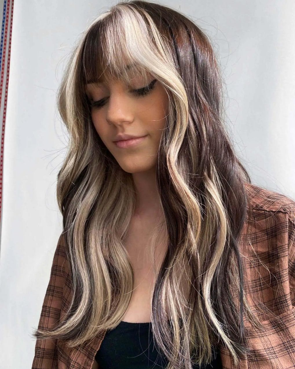 Long-layered cut with ash blonde highlights, full fringe, and soft waves.