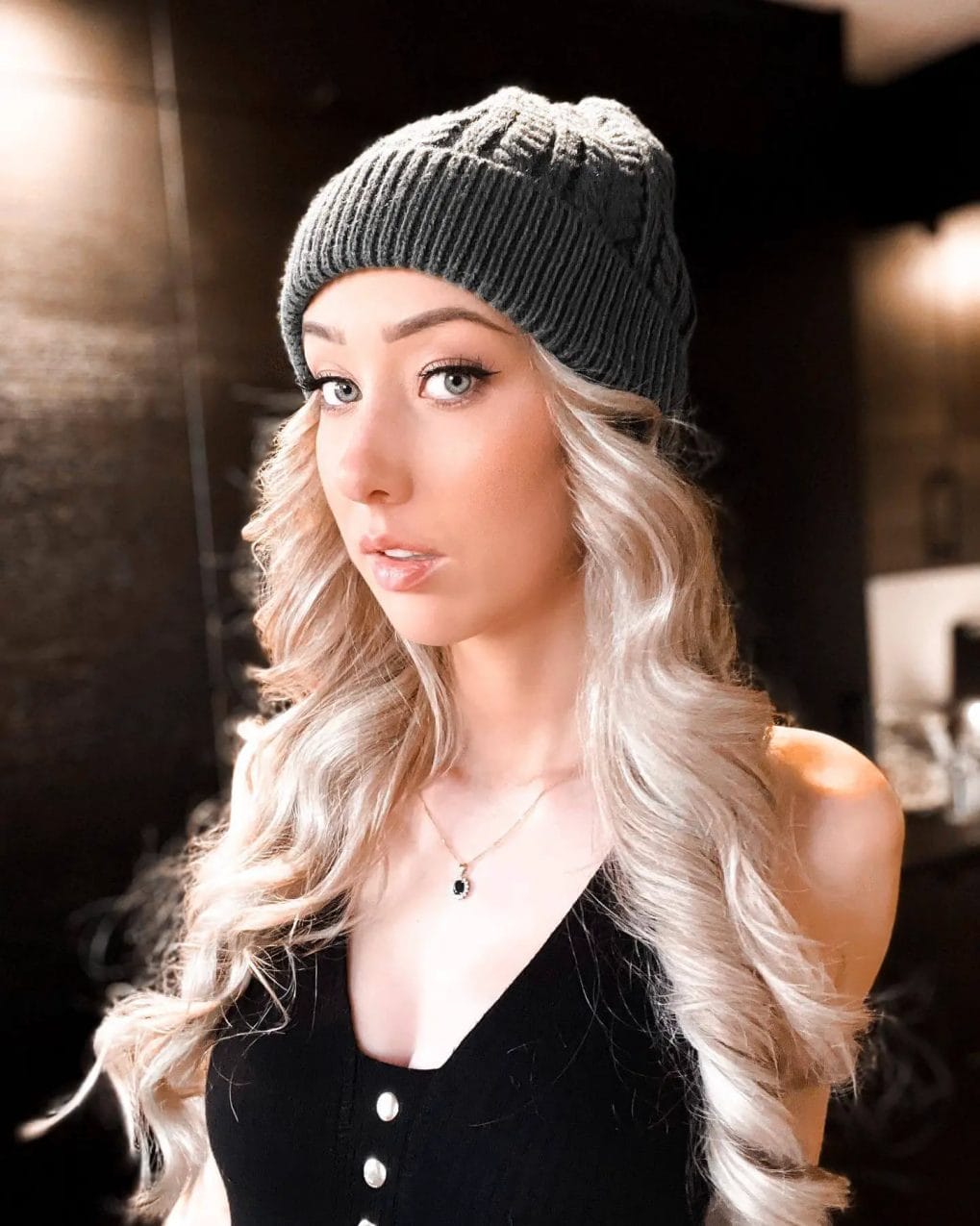 Flowing ash-blonde waves framed by a ribbed charcoal beanie.
