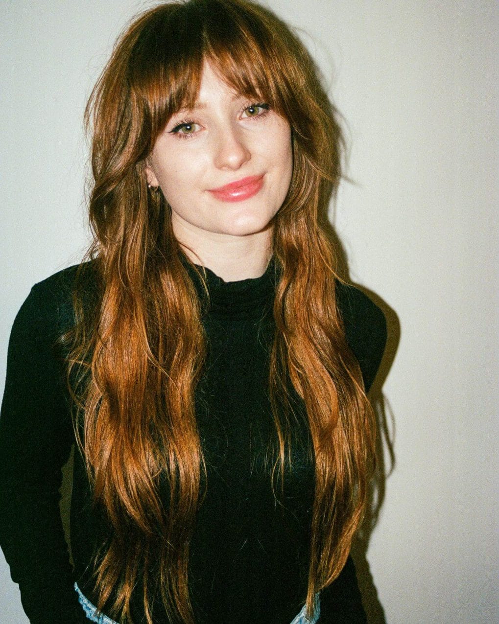 Long auburn waves with light wispy Bardot bangs, evoking a youthful and bohemian aura.