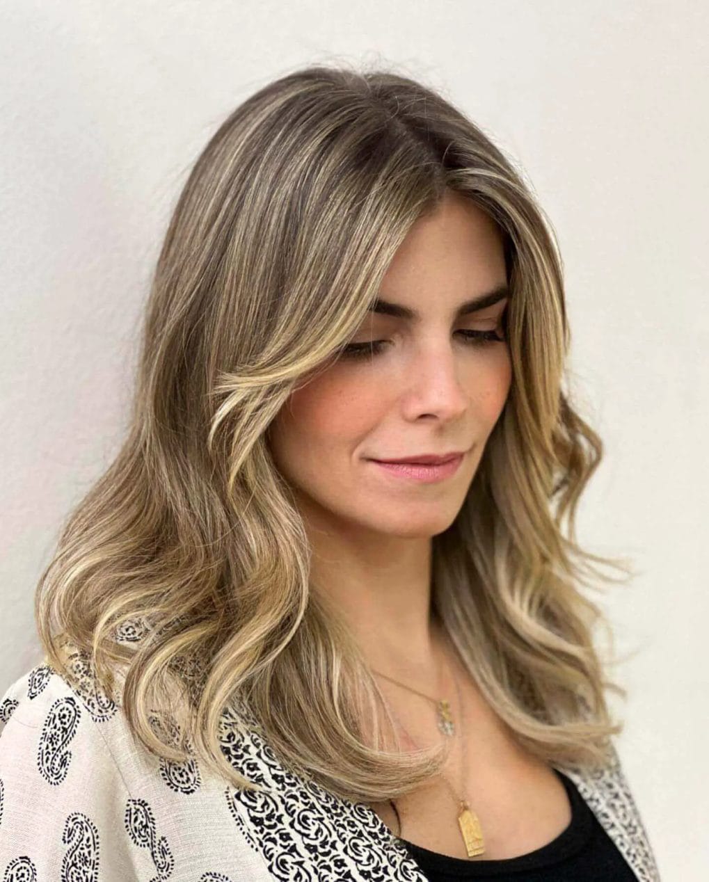 Medium-length hairstyle with natural soft waves and long, sweeping curtain bangs in cool and warm blonde balayage.