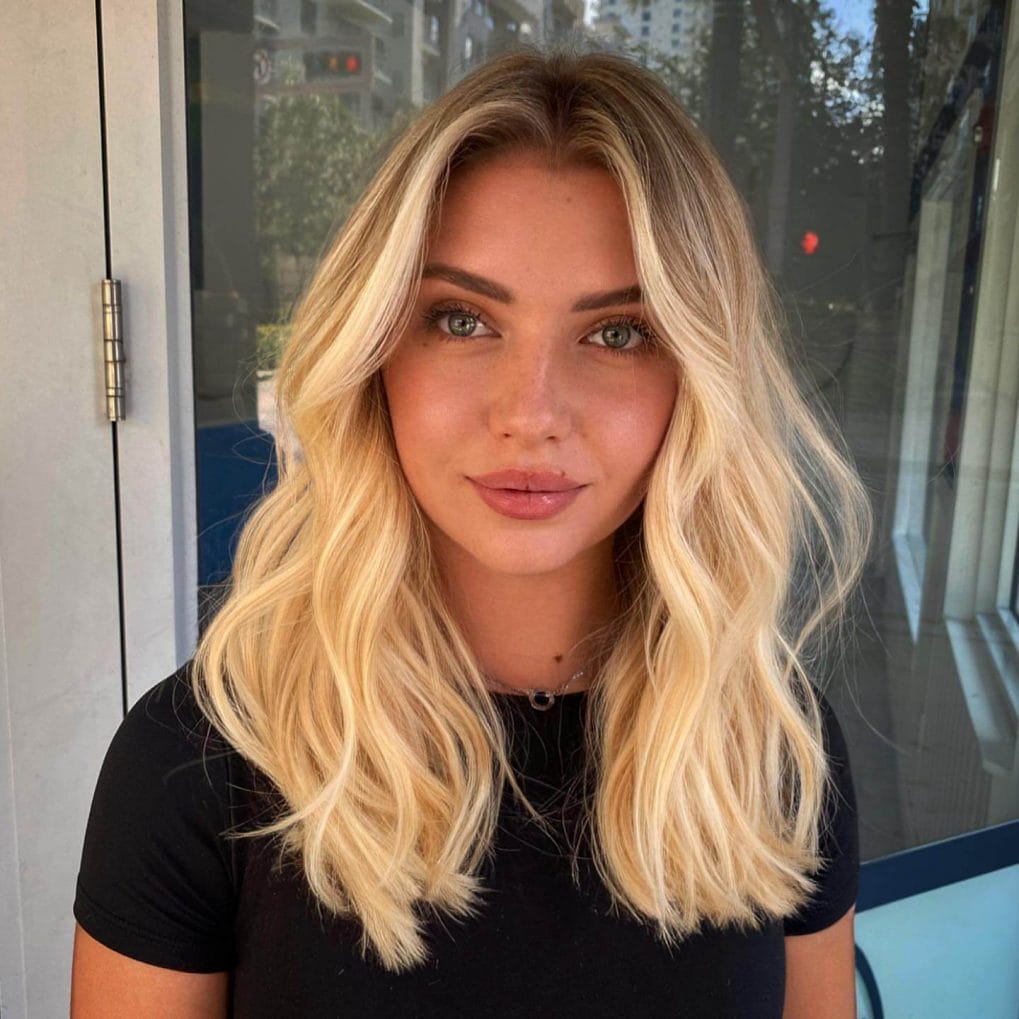 Medium buttery blonde beachy waves with soft curtain bangs and middle parting.