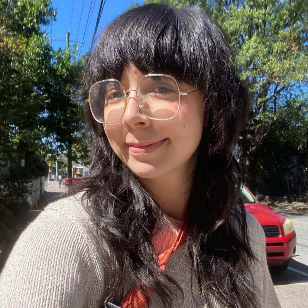Jet-black wavy hair with full fringe and standout glasses.