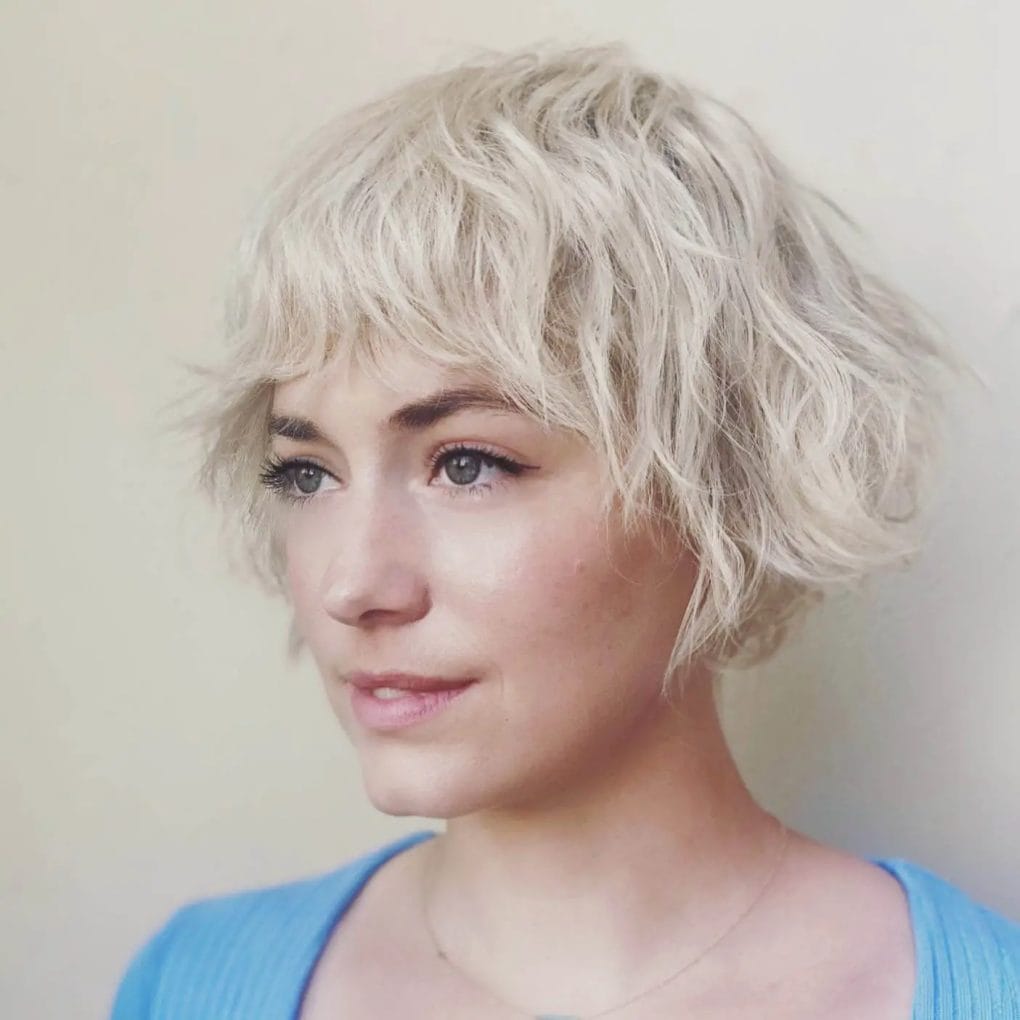 Striking bleached wavy pixie with bold bangs.
