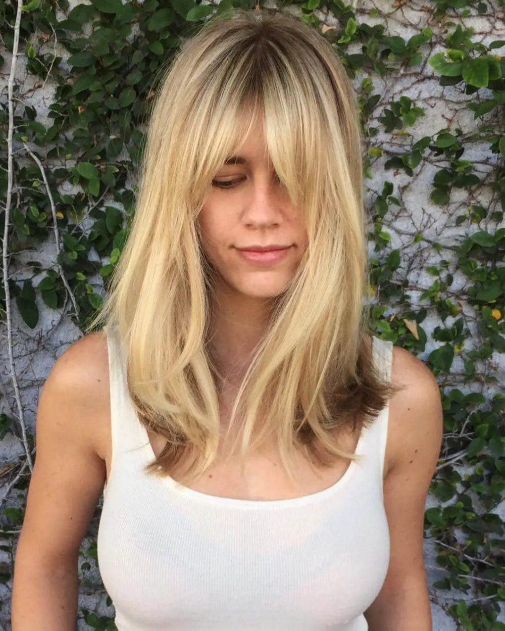Soft blond balayage with layered waves and retro-inspired bardot bangs, blending classic and contemporary.