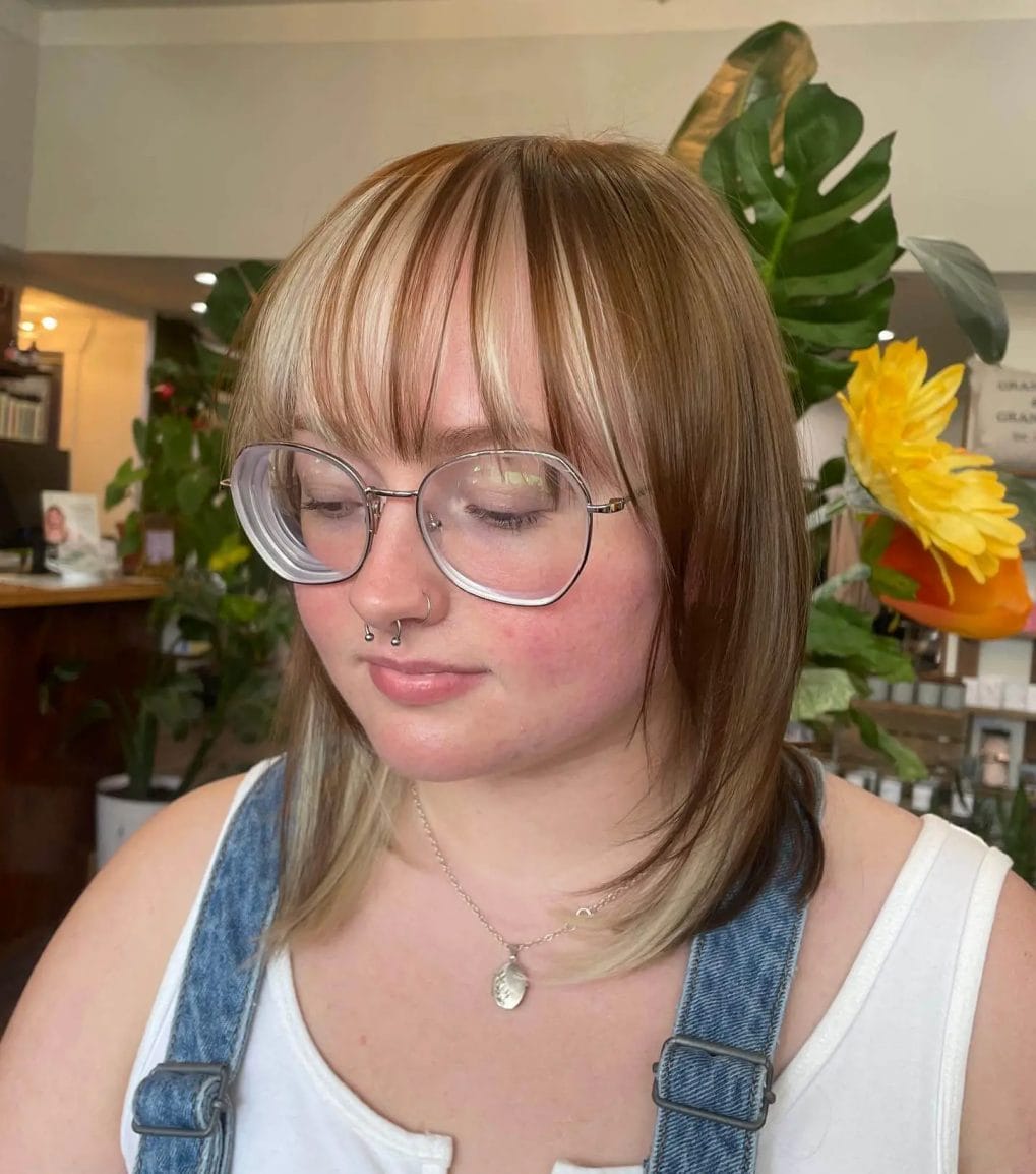Layered blonde bob with piecey bangs and geometric glasses.