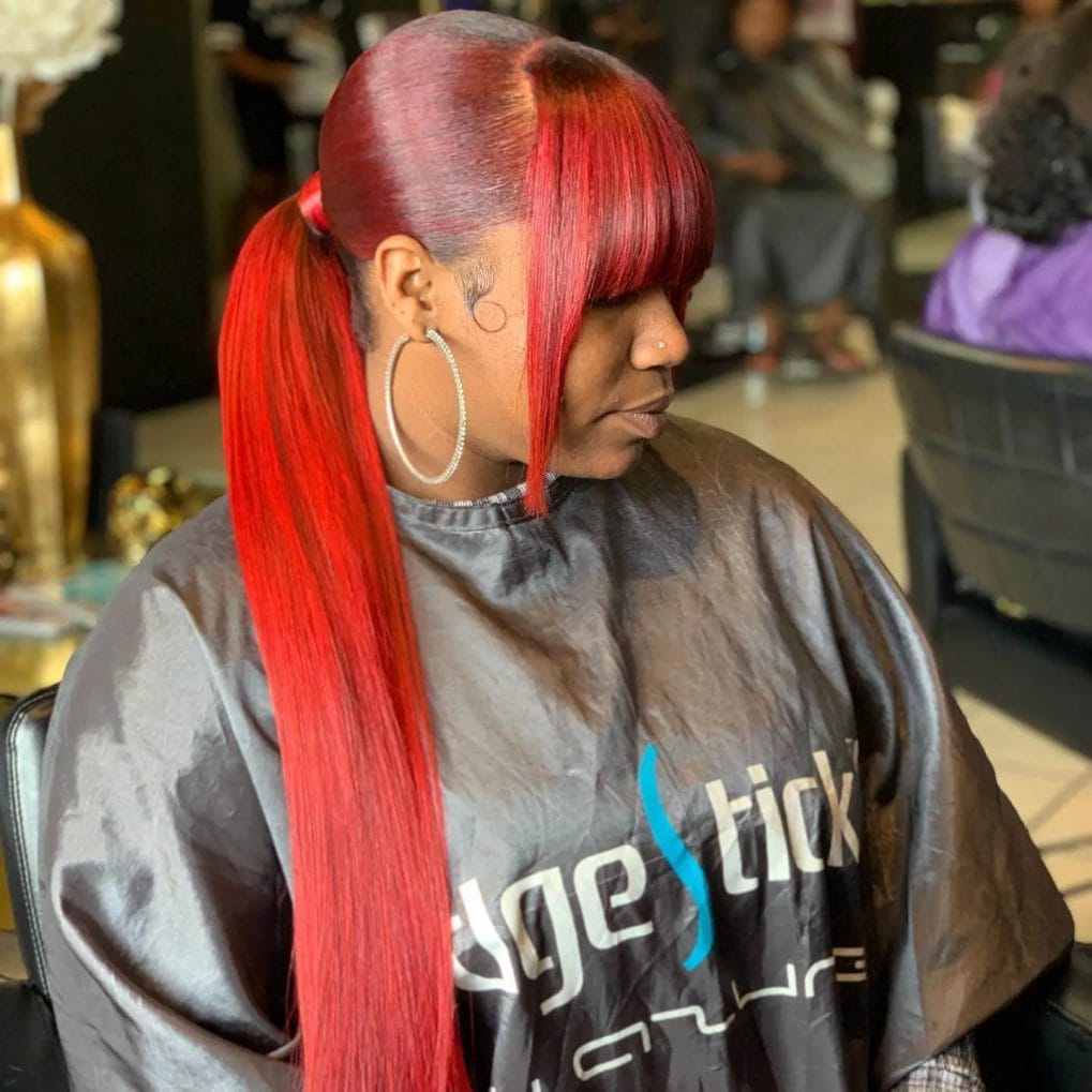 Striking red sleek ponytail with contrasting dark roots and a full blunt fringe for a daring, modern look.