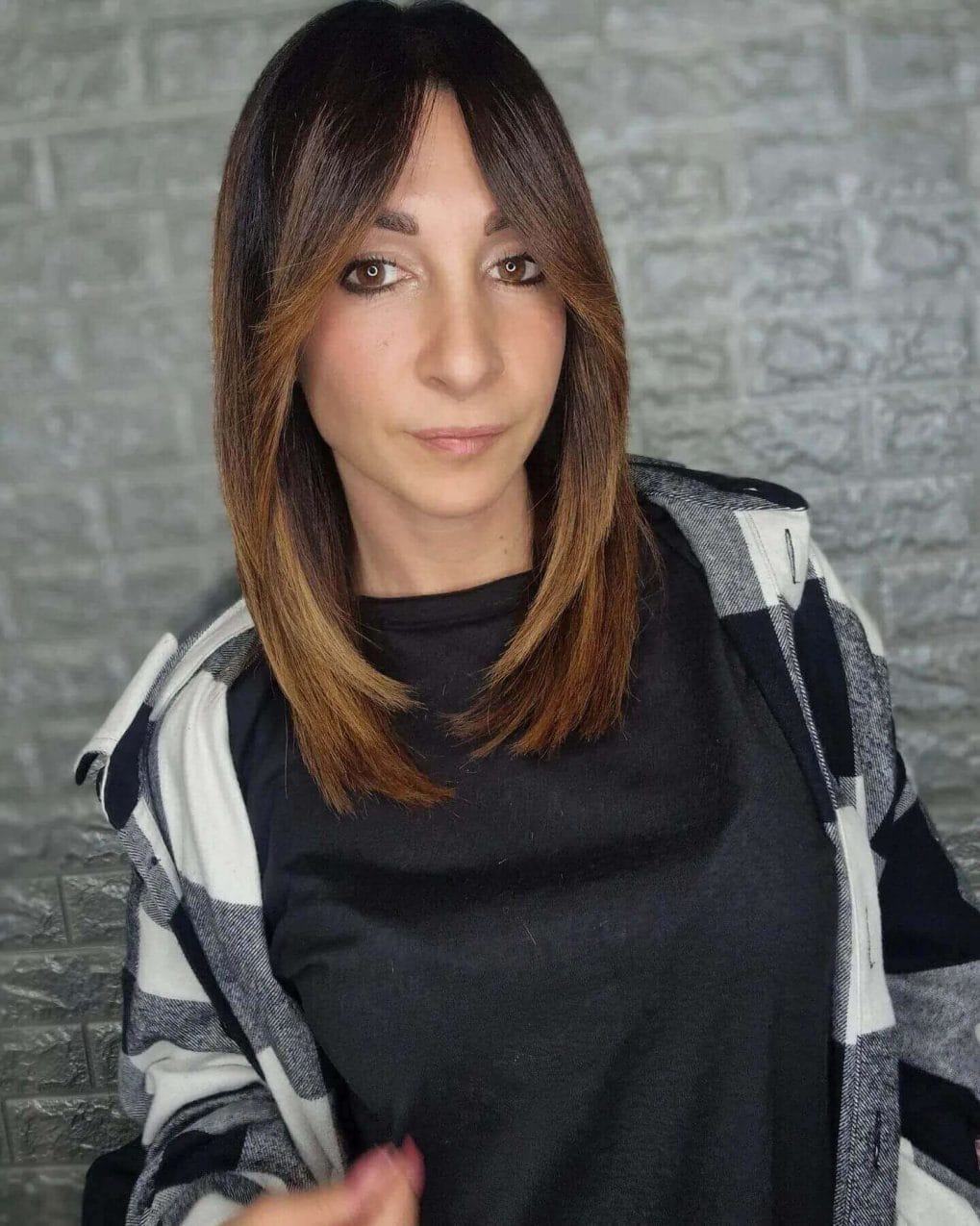 Chic medium-length straight hair with dark roots and warm caramel ombre, complemented by long feathered bangs.