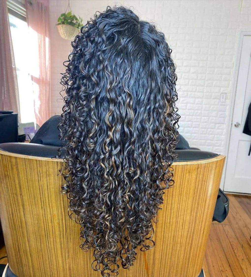 Curly long hair with balayage highlights in a V-shaped cut.