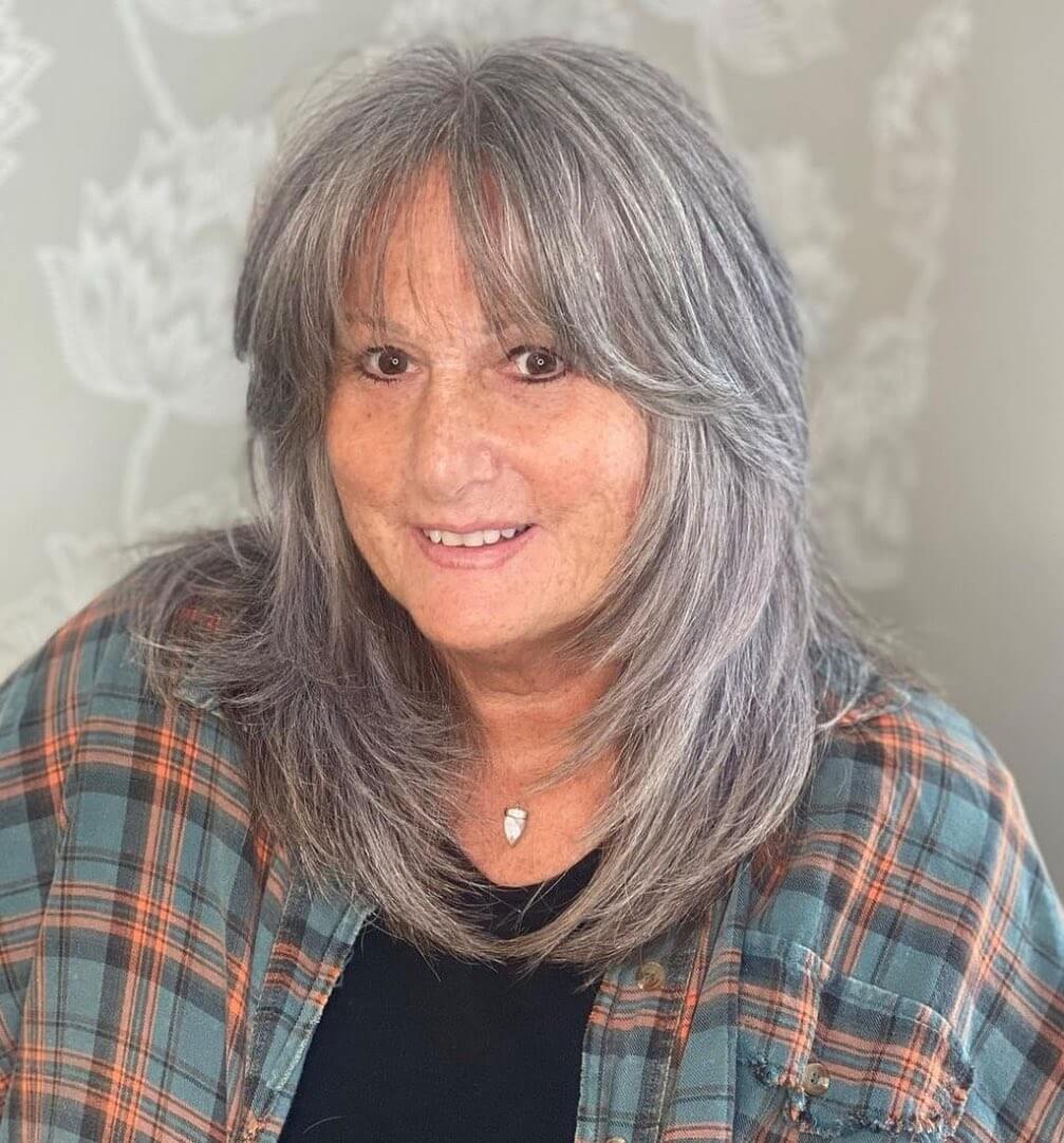 Breezy medium-length gray hair with brown streaks and gentle waves.