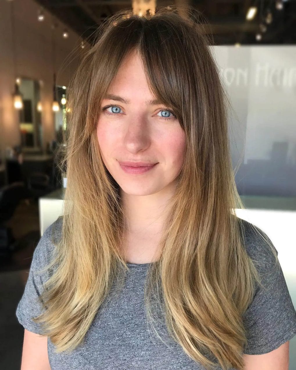 Layered locks with a sun-kissed ombre transitioning from deep brown, complemented with curtain bangs.