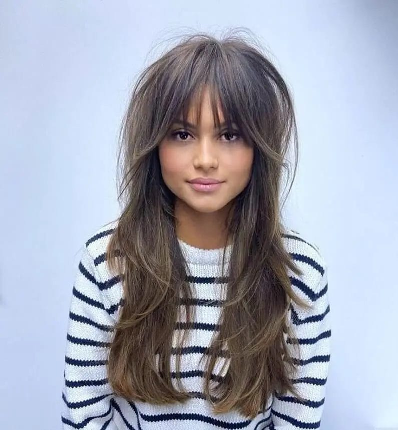 Rich brunette with layered blowout and a mix of curtain and bardot bangs, offering a timeless trendy look.