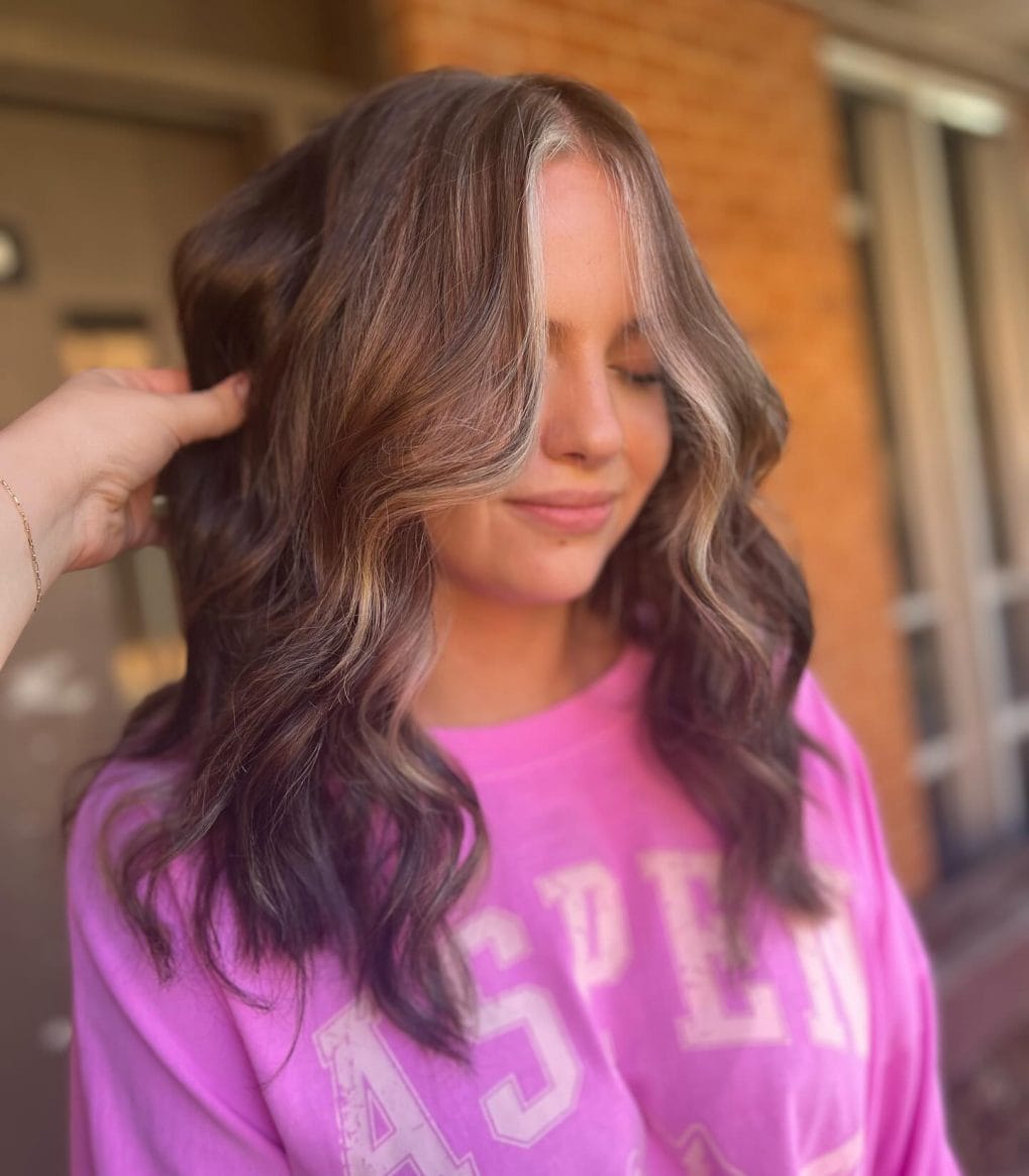 Brown hair with playful waves and light-hued money piece framing the face