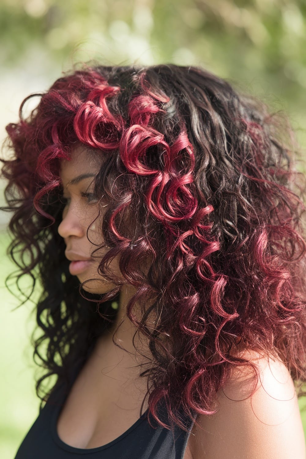 Profile view of a woman with natural curly hair featuring burgundy highlights.