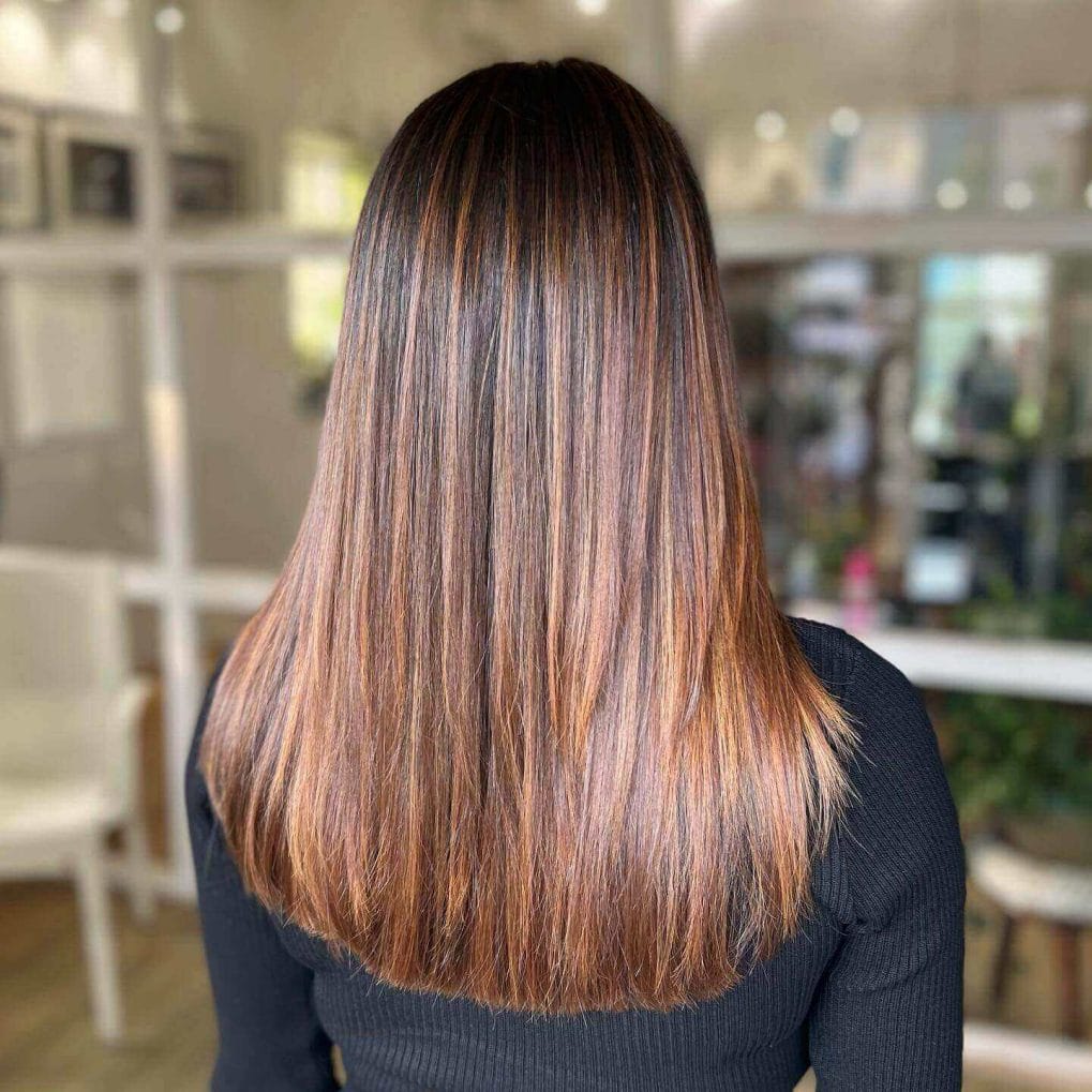 Mid-back length straight hair with warm caramel balayage on dark base.