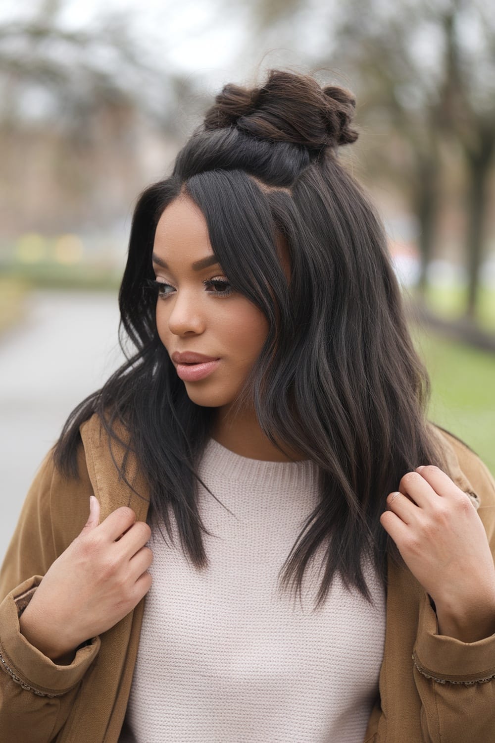 A young woman with a half up messy bun hairstyle, looking stylish and relaxed outdoors.