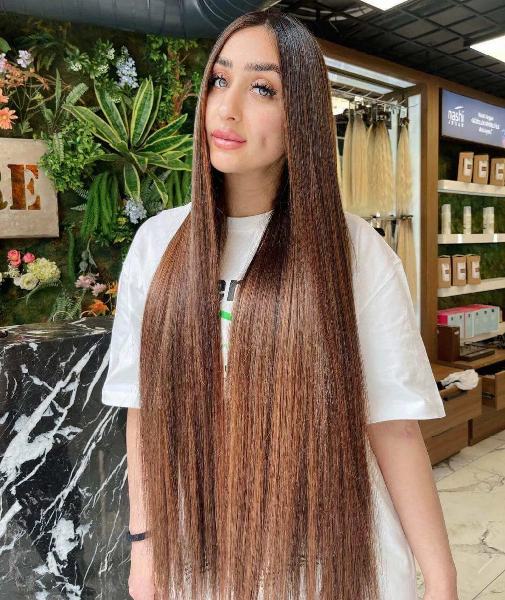 Long straight hair with chestnut and honey balayage and center-parted fringe.
