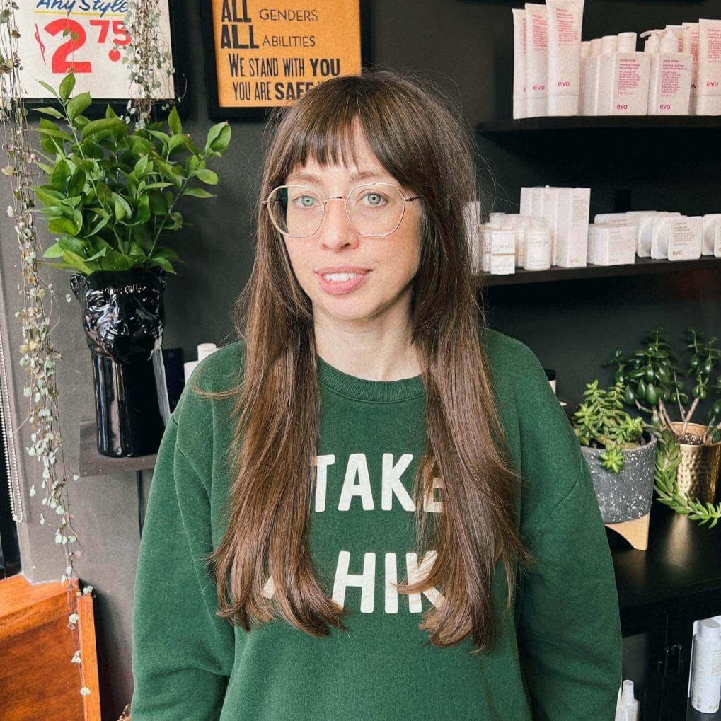 Long chestnut layers with see-through fringe and round glasses frames.
