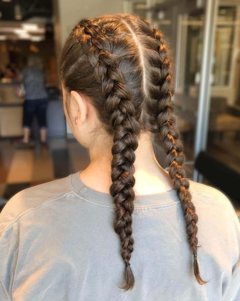 Neatly crafted chestnut braids forming twin ponytails, loosening towards the ends.