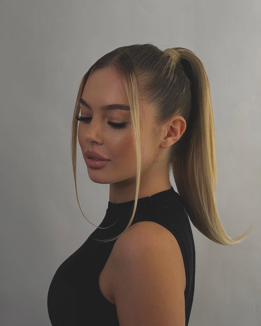 Chic high ponytail in glossy blonde, with sleek side-parted strands merging into the ponytail for a modern twist.