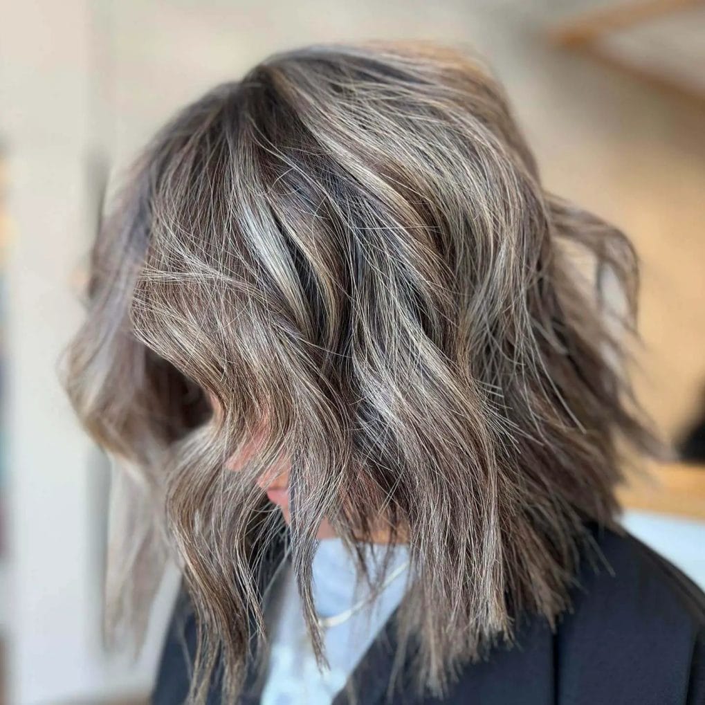 Choppy, tousled bob with airy curtain bangs in ash and honey tones.