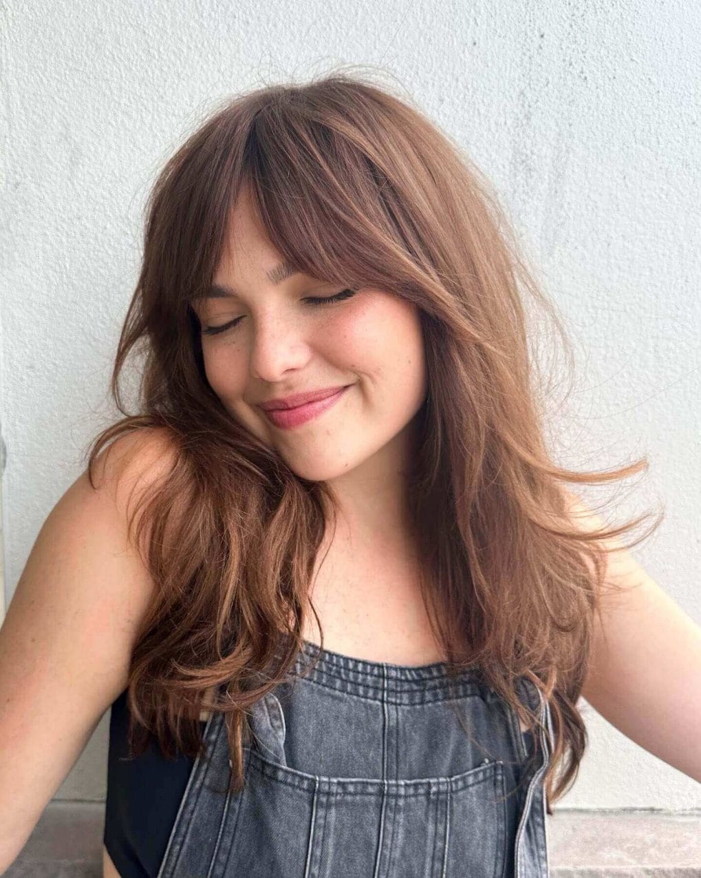 Medium cinnamon shaded hair with seamless layers and full, sweeping curtain bangs.