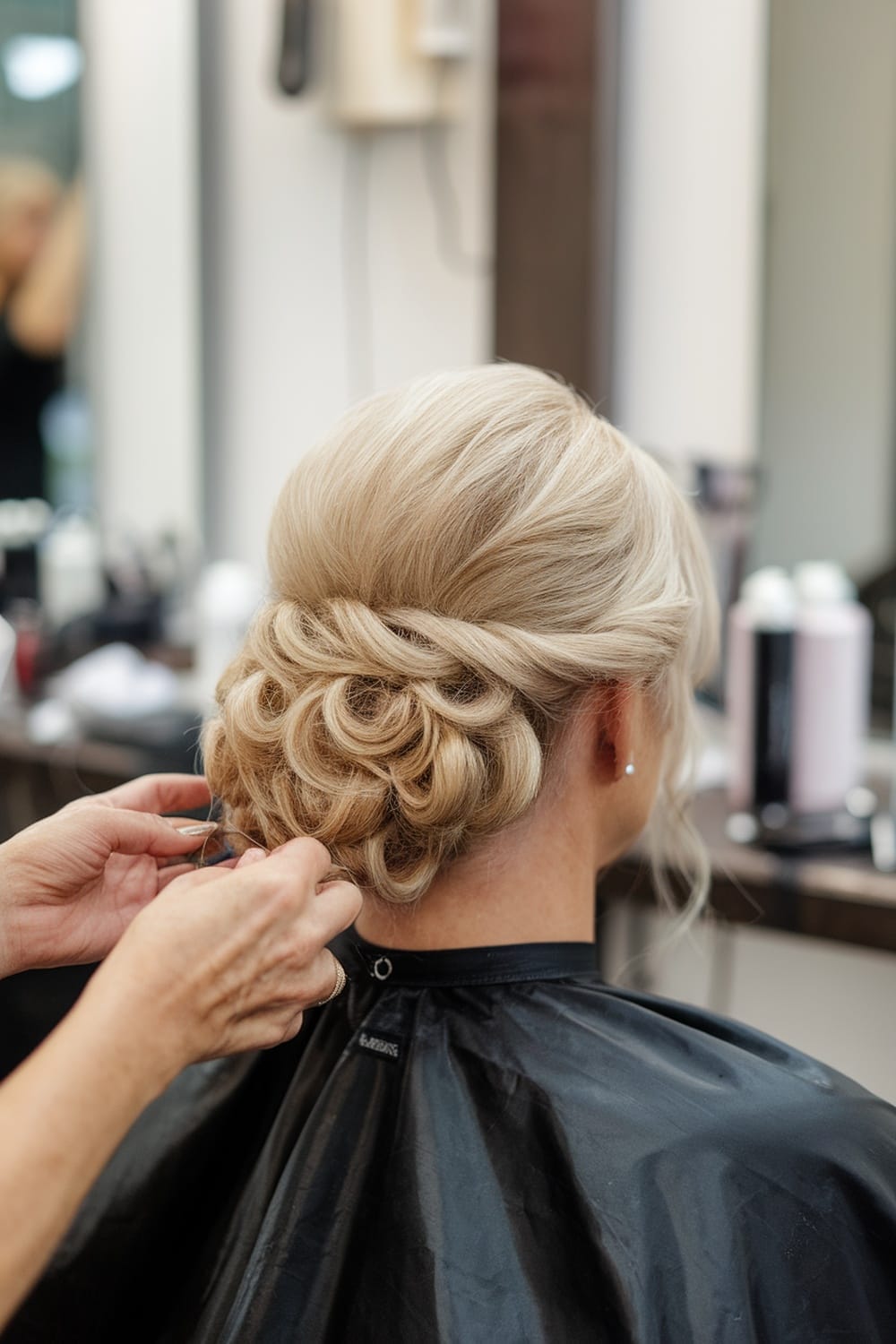 A stylist arranging a classic French twist hairstyle for the mother of the bride.