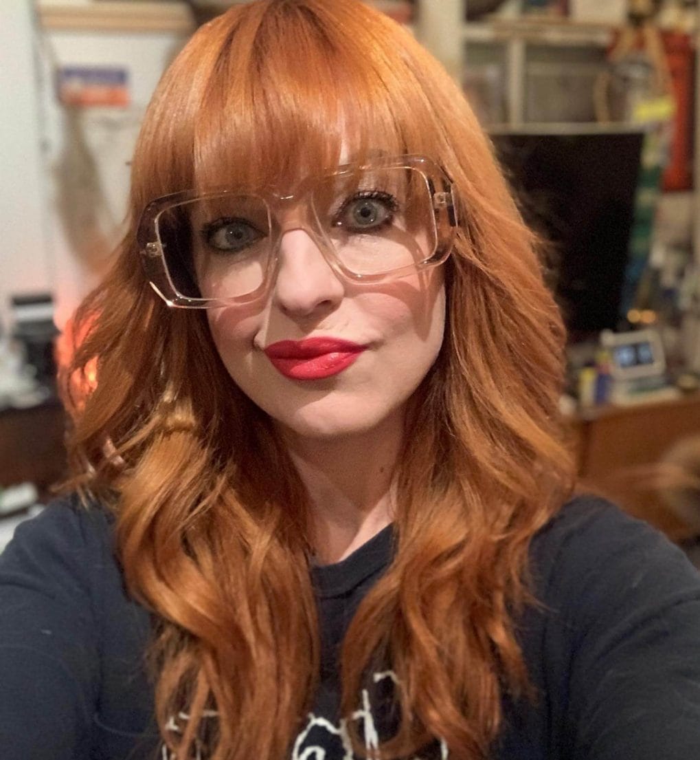Vibrant copper bouncy waves with full bangs and retro glasses.