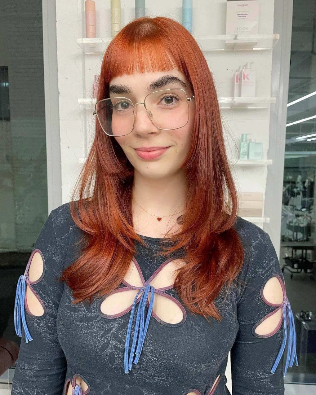 Mid-length fiery copper curls with blunt fringe and minimalist glasses.