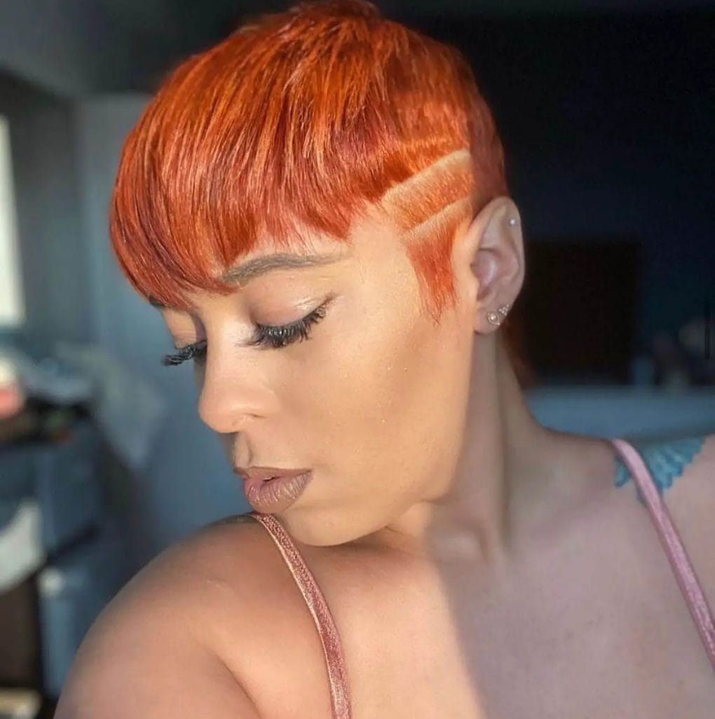 Vibrant copper pixie with full, side-swept bangs and an undercut featuring carved lines.
