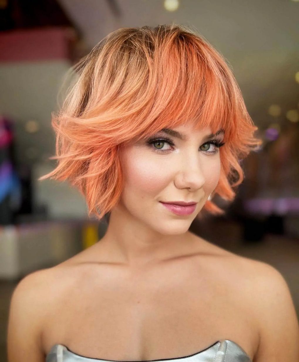 Vibrant coral bixie with blonde highlights, layered with volume and complemented by bangs.