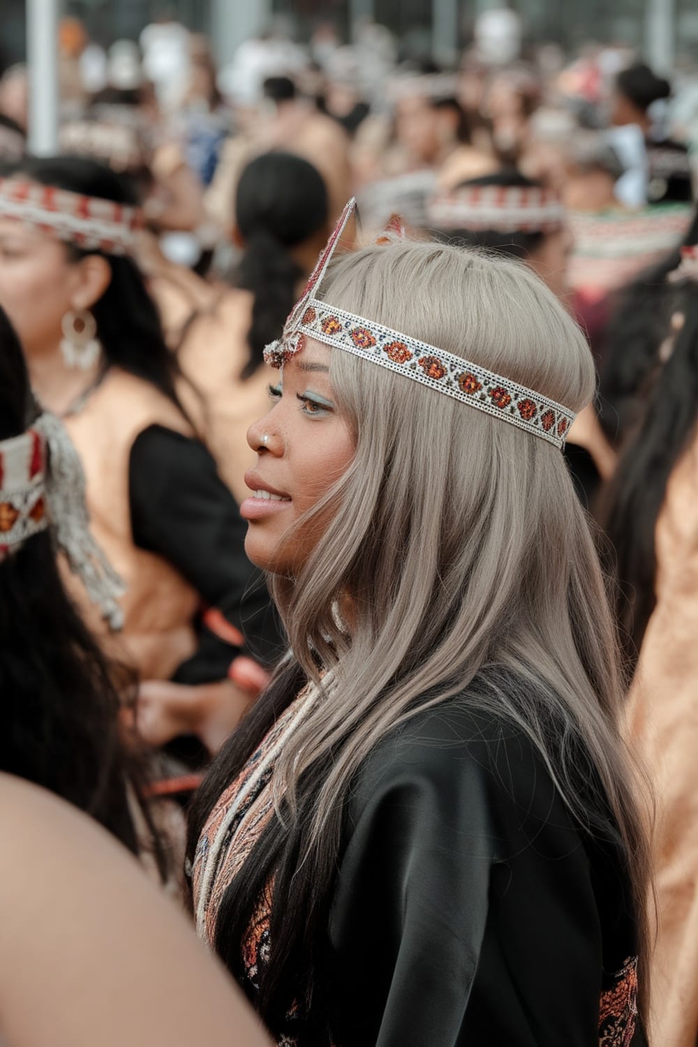 A woman with ash blonde hair styled elegantly, wearing traditional attire and adorned with a decorative headpiece, amidst a gathering.