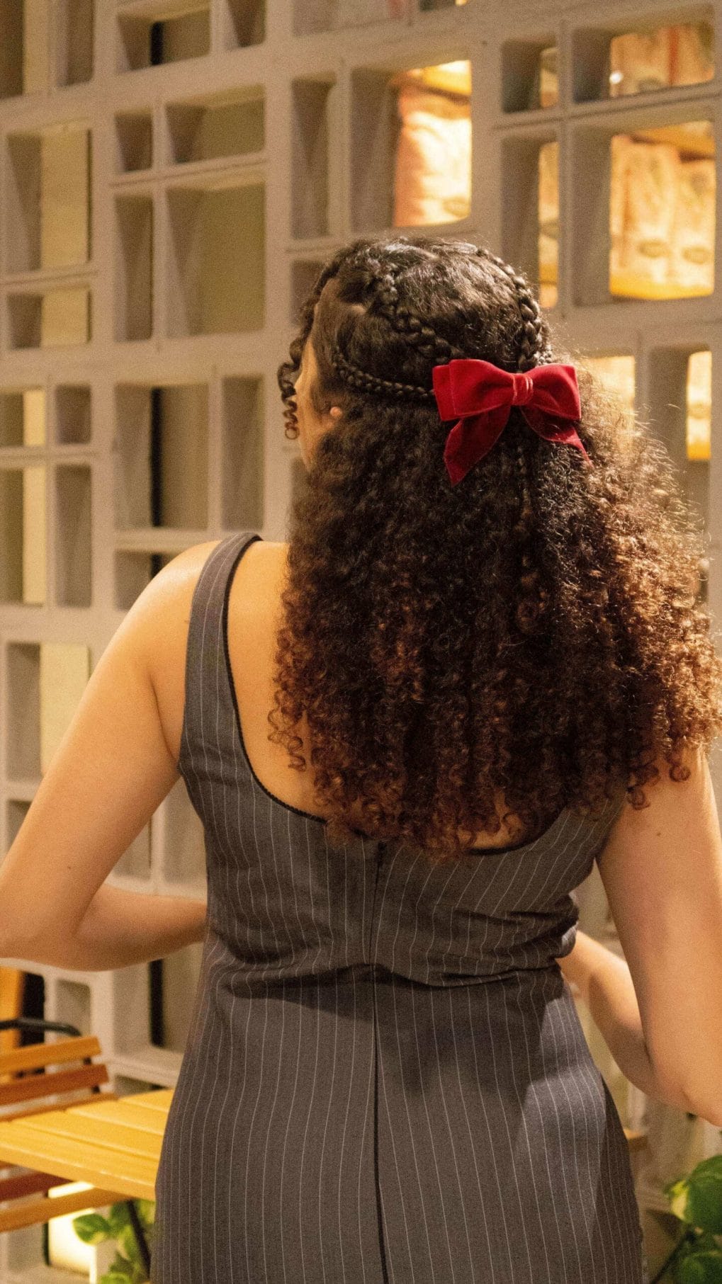 Braided crown with curly ponytail adorned by a bold red bow in natural tones