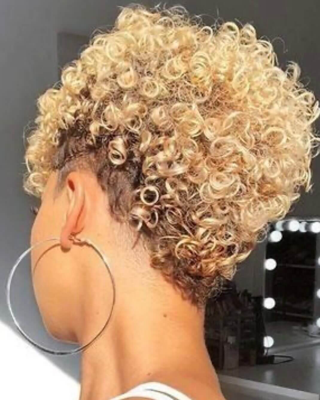 Curly tapered cut with dark roots and golden tips.