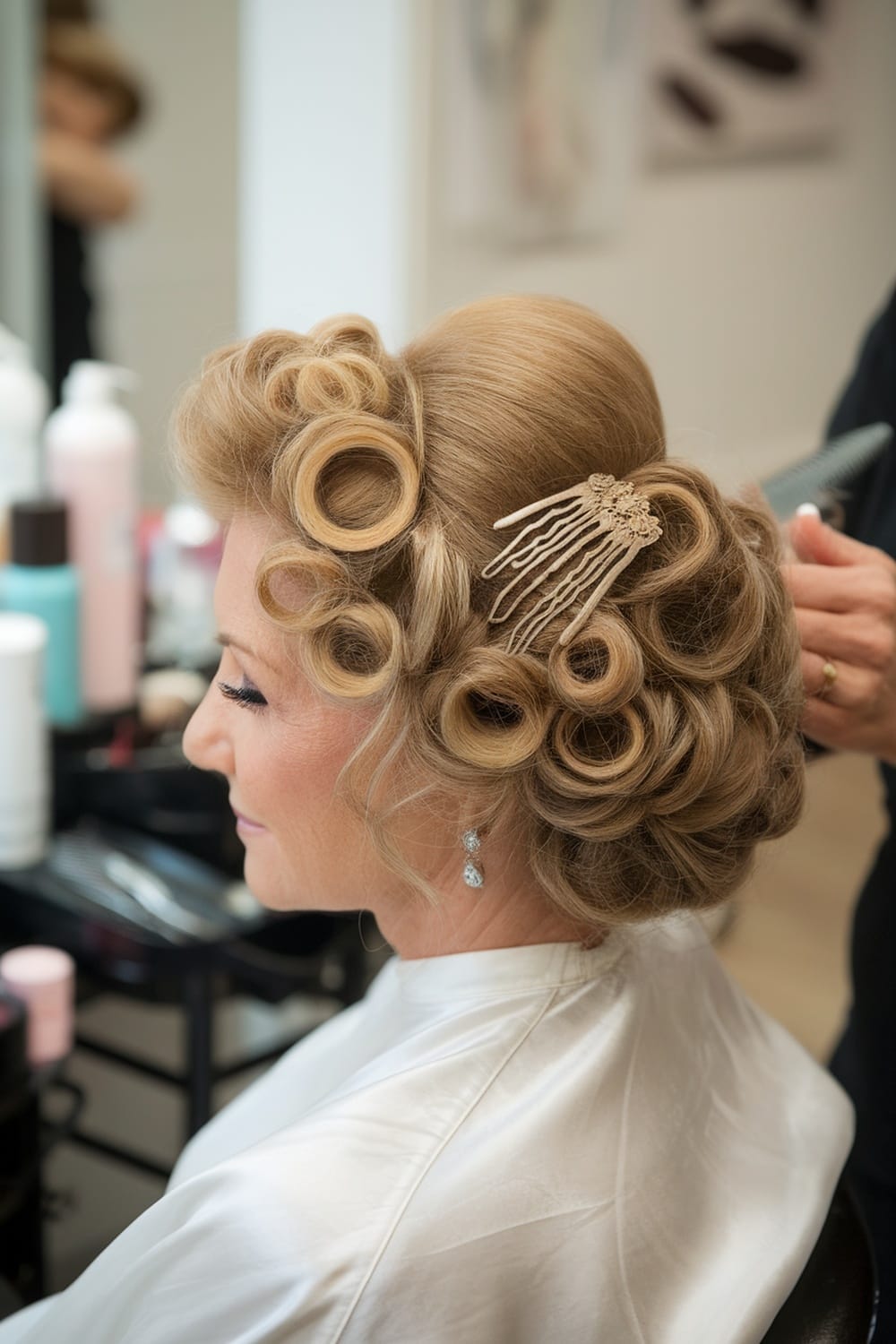 A woman with a curly updo hairstyle adorned with vintage hair combs, sitting in a salon.