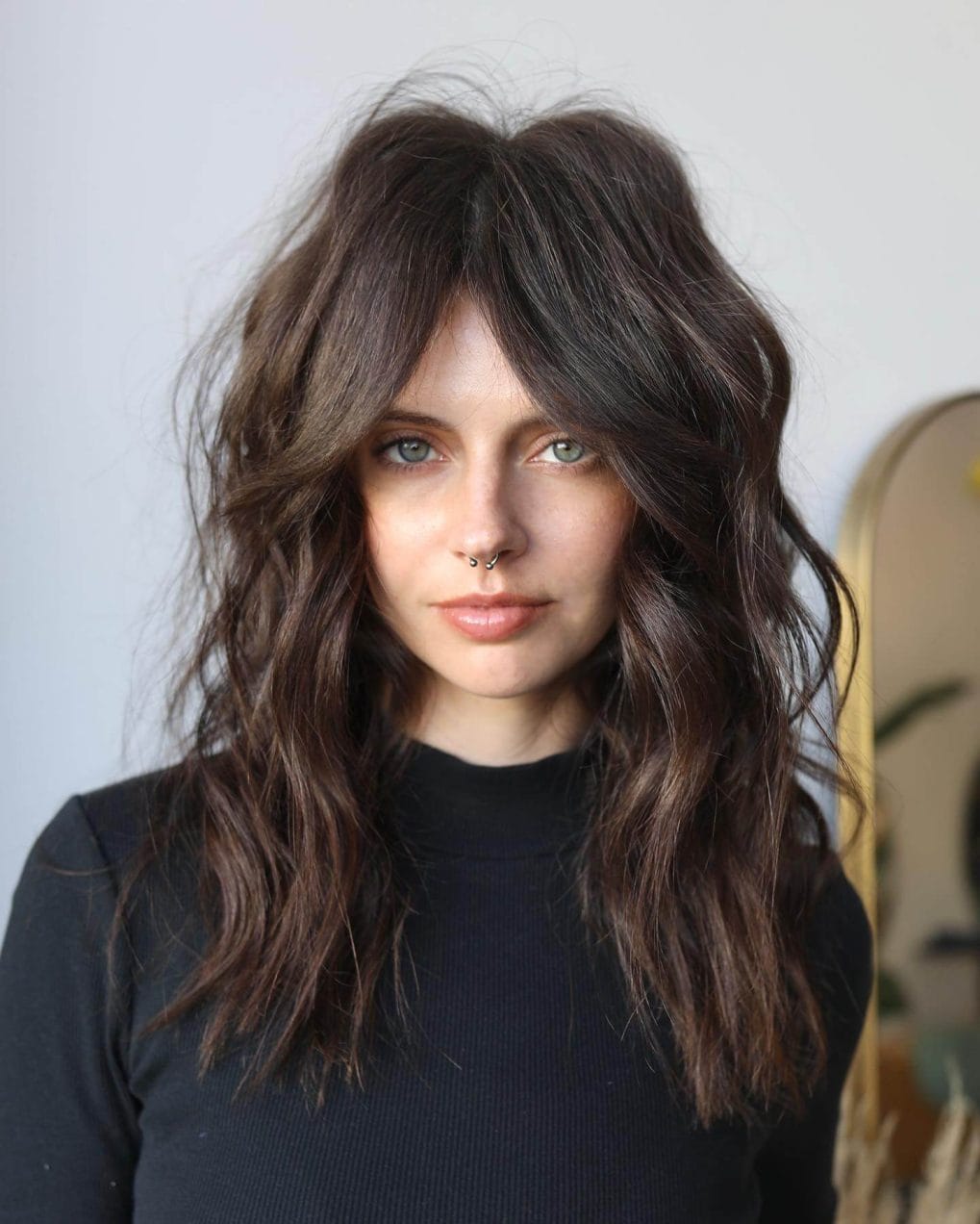 Relaxed medium dark chocolate shaggy cut with tousled waves and trendy curtain bangs.