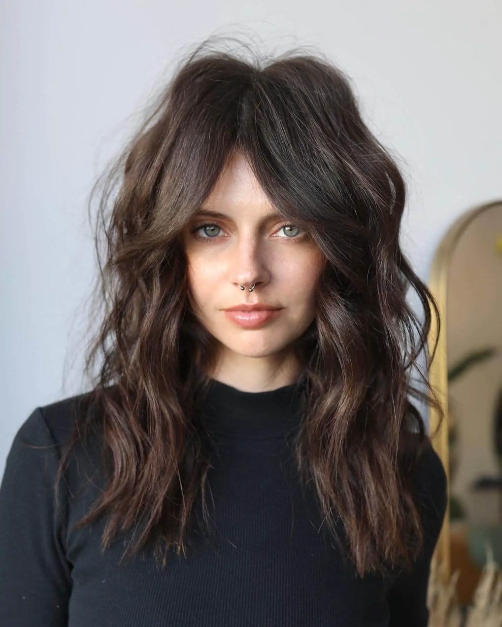 Relaxed medium dark chocolate shaggy cut with tousled waves and trendy curtain bangs.