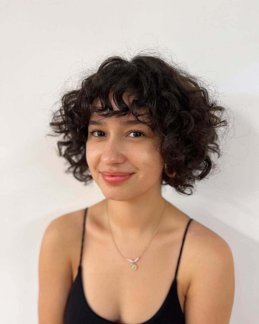 Delightful chin-length bob with dark curls and feathered bangs.
