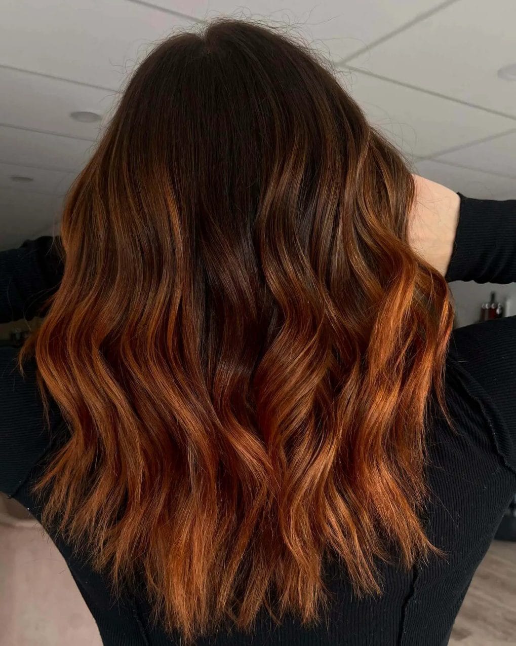 Dimensional copper hair transitioning from dark roots to fiery ends with bouncy waves.