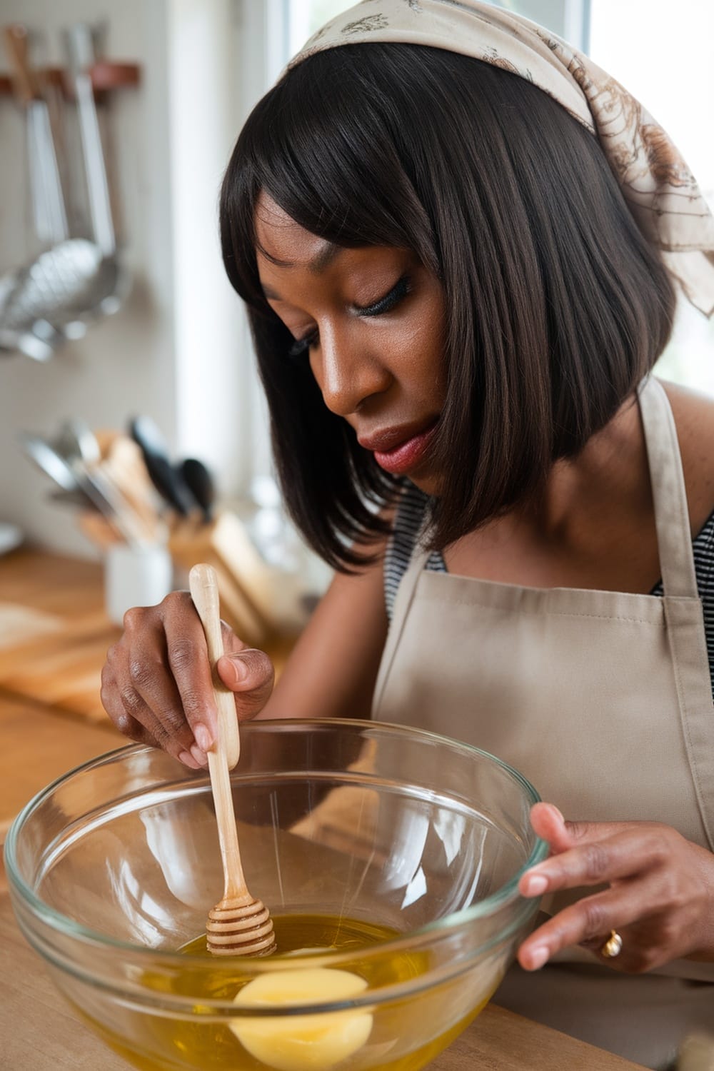 A woman preparing a DIY hair treatment in a kitchen setting, focused on mixing honey with oil in a bowl.