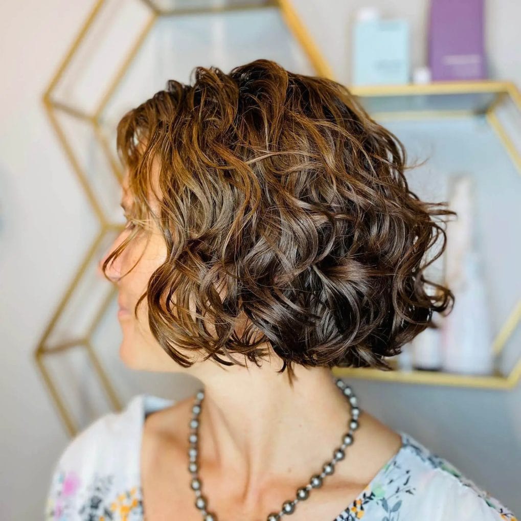 Short haircut with curly perm waves and interplay of dark and light tones.